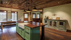 A kitchen with wooden cabinets, a central island, pendant lighting, and a coffee-themed wall decoration. - Entire Home at Melissa's Farmstead (Fredericksburg)