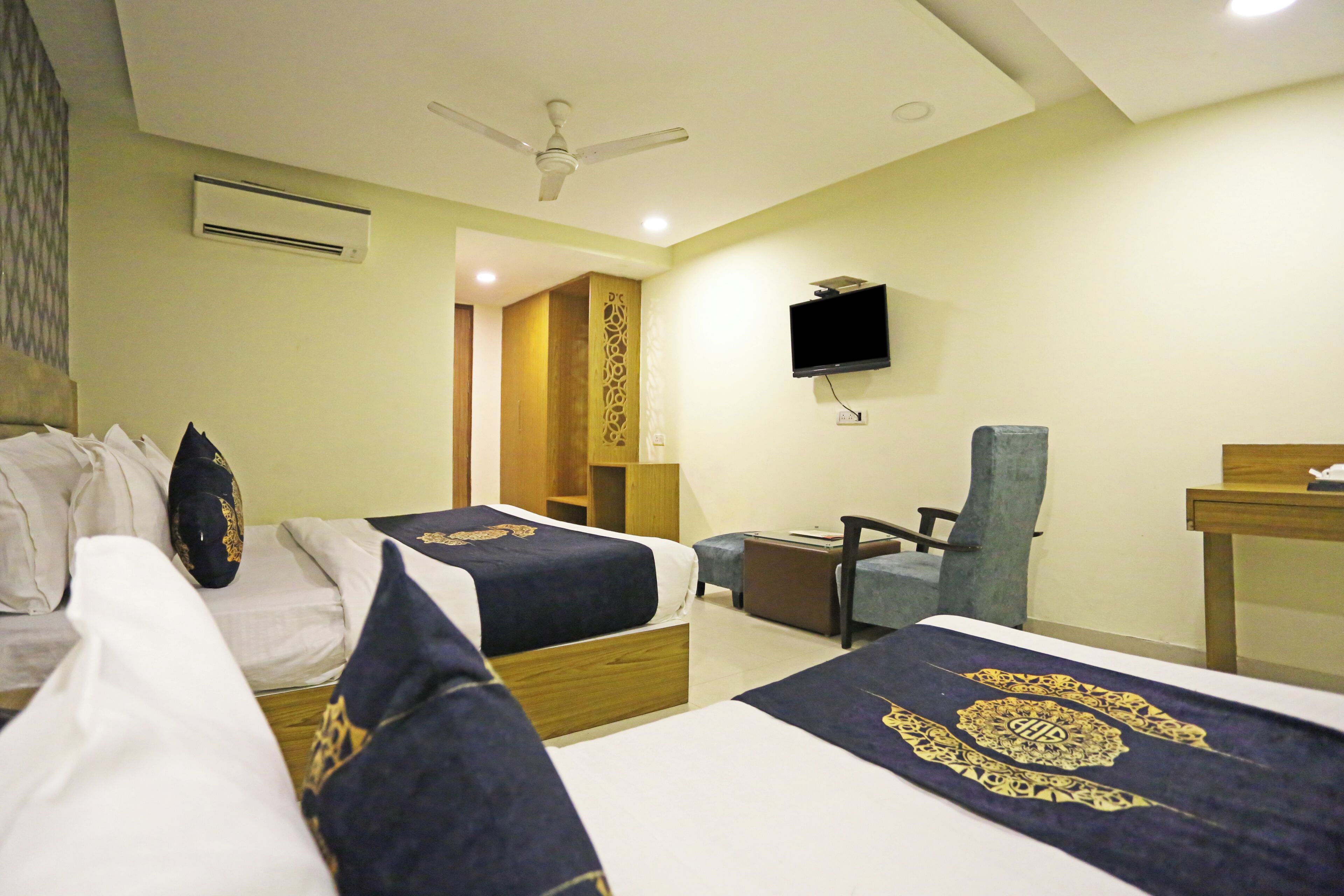 A hotel room with two beds, a desk, a chair, a television, and an air conditioning unit.