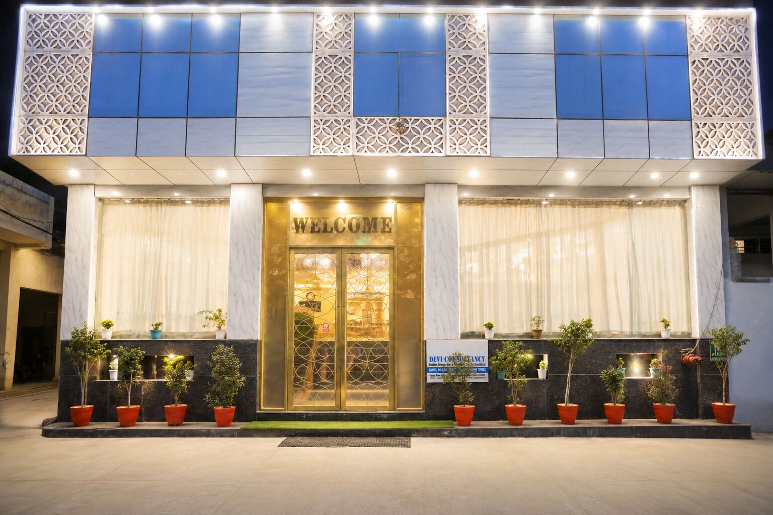 A hotel entrance with a 'WELCOME' sign, potted plants, and a signboard for 'DEV CONSULTANCY'.