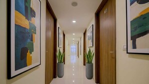 A hallway with framed artwork on the walls, potted plants, and wooden doors. - The D'Capitol Delhi, International Airport (New Delhi)