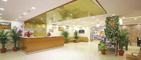 A hotel lobby with a reception desk, seating area, potted plants, and a brick accent wall.
