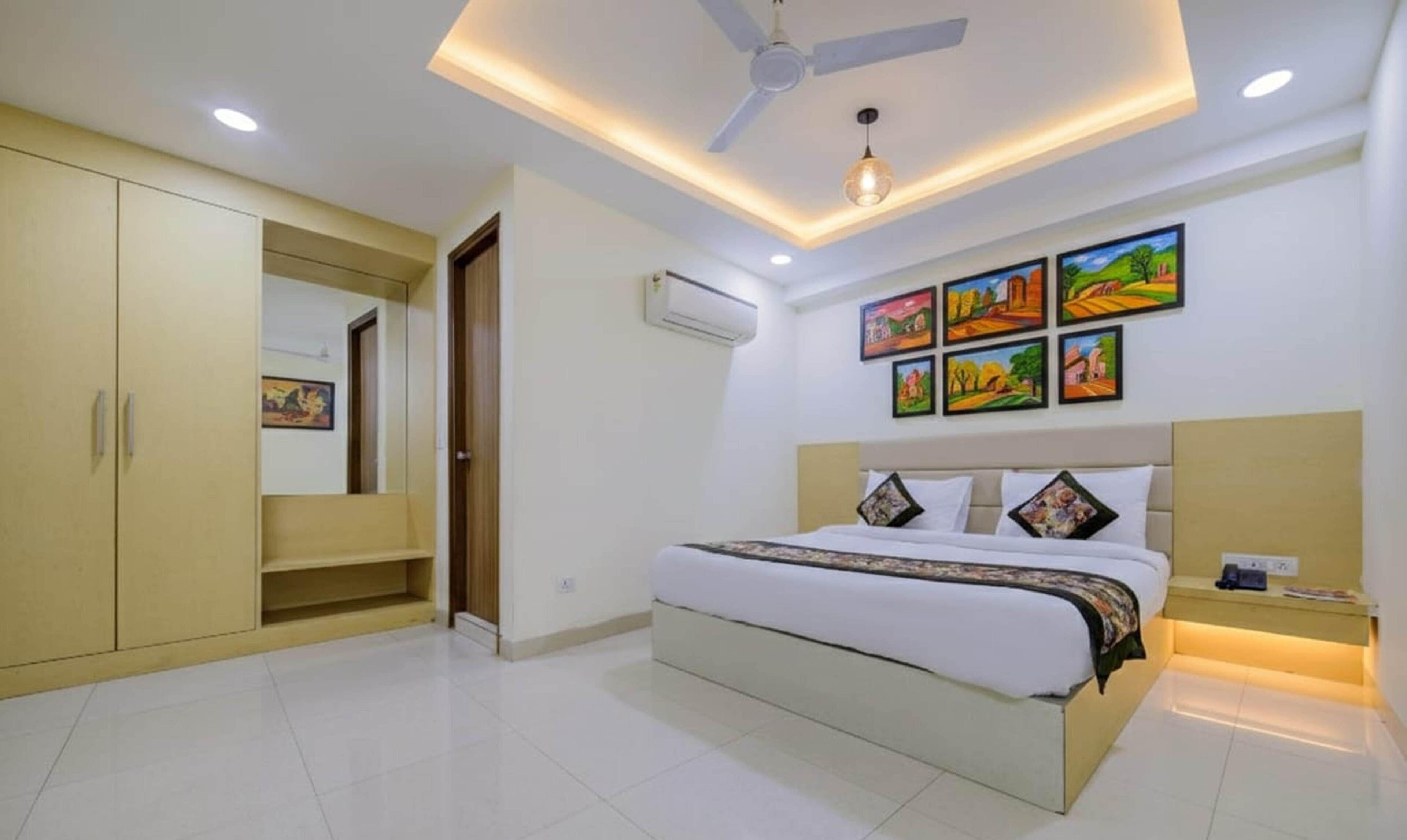 A bedroom with a bed, a ceiling fan, recessed lighting, an air conditioner, and a series of paintings on the wall.