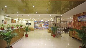 A hotel lobby with a reception desk, seating area, and a wall with a clock and a sign. - The D'Capitol Delhi, International Airport (New Delhi)