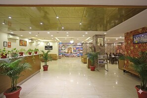 A hotel lobby with a reception desk, seating area, and a wall with a clock and a sign. - The D'Capitol Delhi, International Airport (New Delhi)