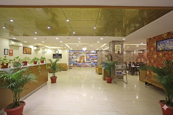 Un hall de hotel con una recepción, zona de estar y una pared con un reloj y un letrero.