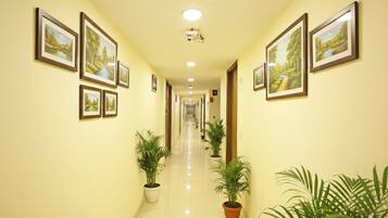 A hotel corridor with framed landscape paintings on the walls, potted plants, and a long, straight hallway.