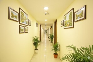 A hotel corridor with framed landscape paintings on the walls, potted plants, and a long, straight hallway. - The D'Capitol Delhi, International Airport (New Delhi)