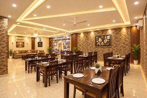 A hotel dining area with multiple tables, chairs, and a seating area with a sofa and a clock. - The D'Capitol Delhi, International Airport (New Delhi)