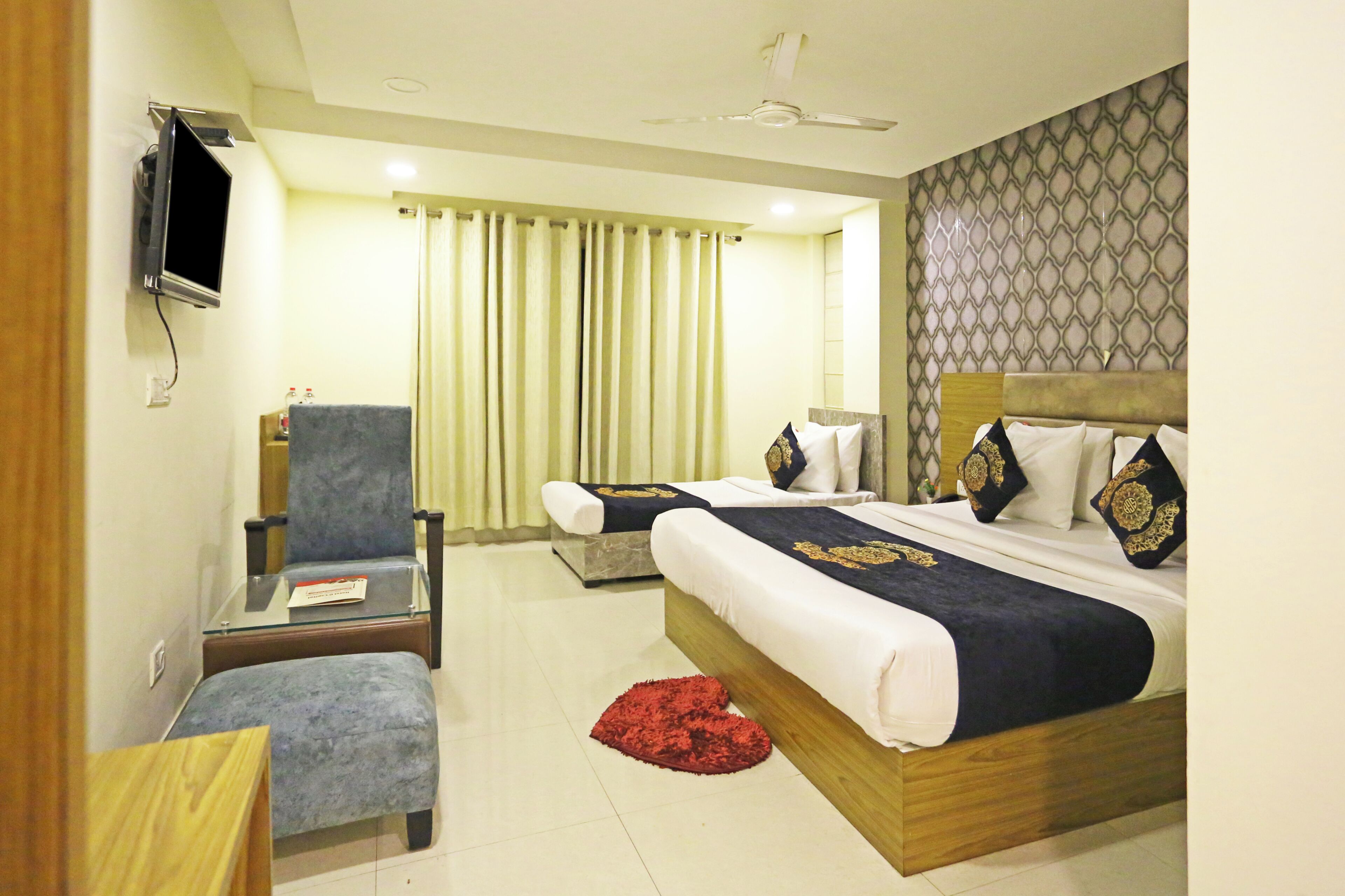 A hotel room with a bed, two chairs, a TV, and a window with curtains.