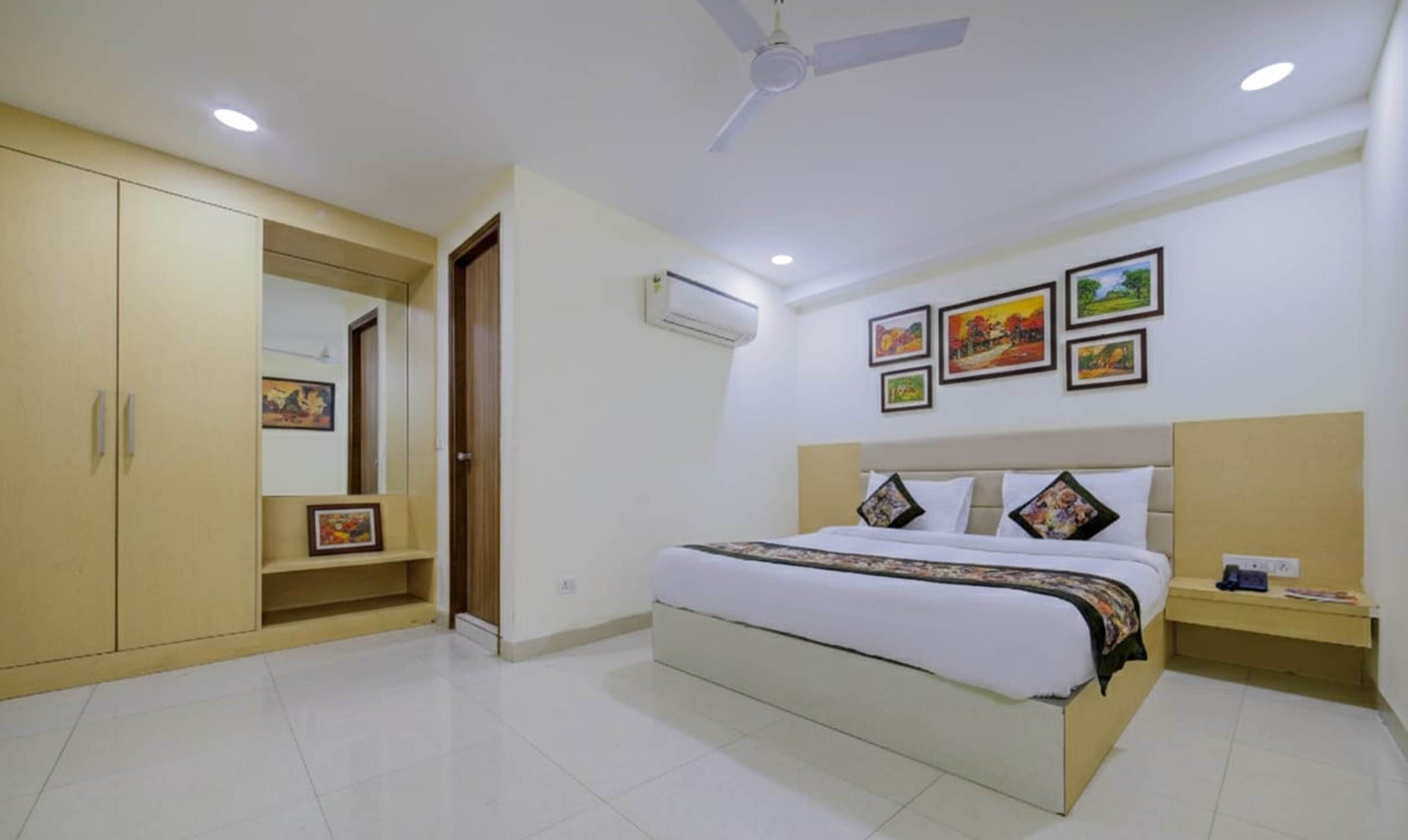 A bedroom with a bed, a wardrobe, a ceiling fan, an air conditioner, and framed pictures on the wall.