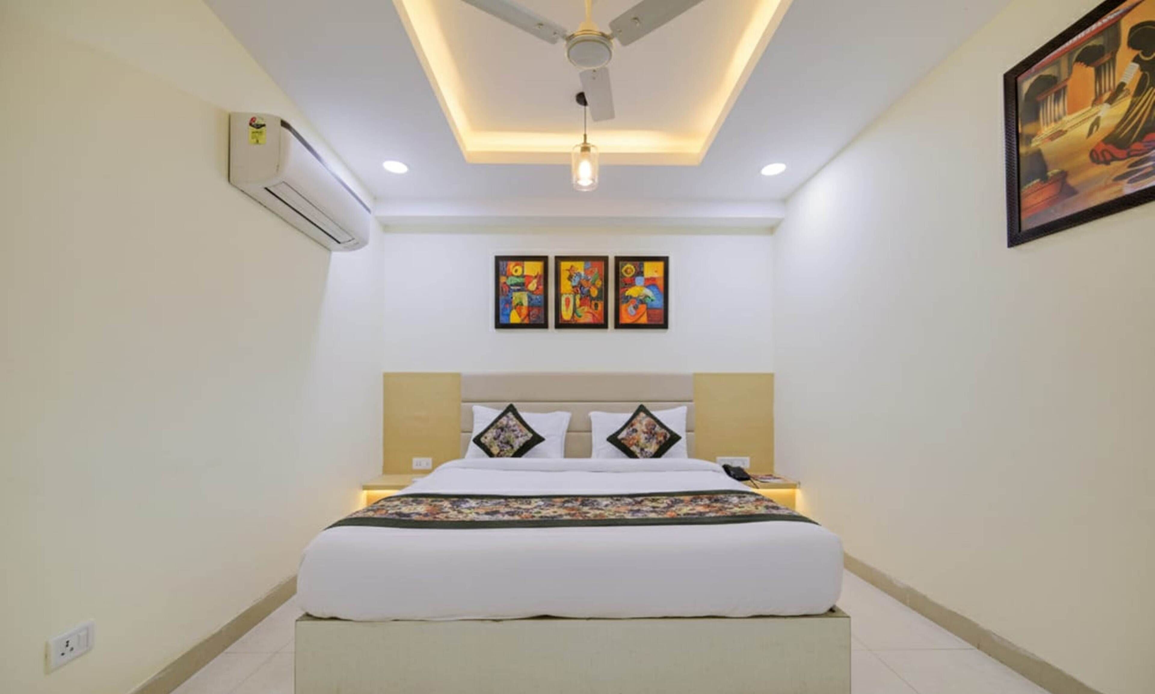A bedroom with a bed, ceiling fan, air conditioning unit, and three paintings on the wall.