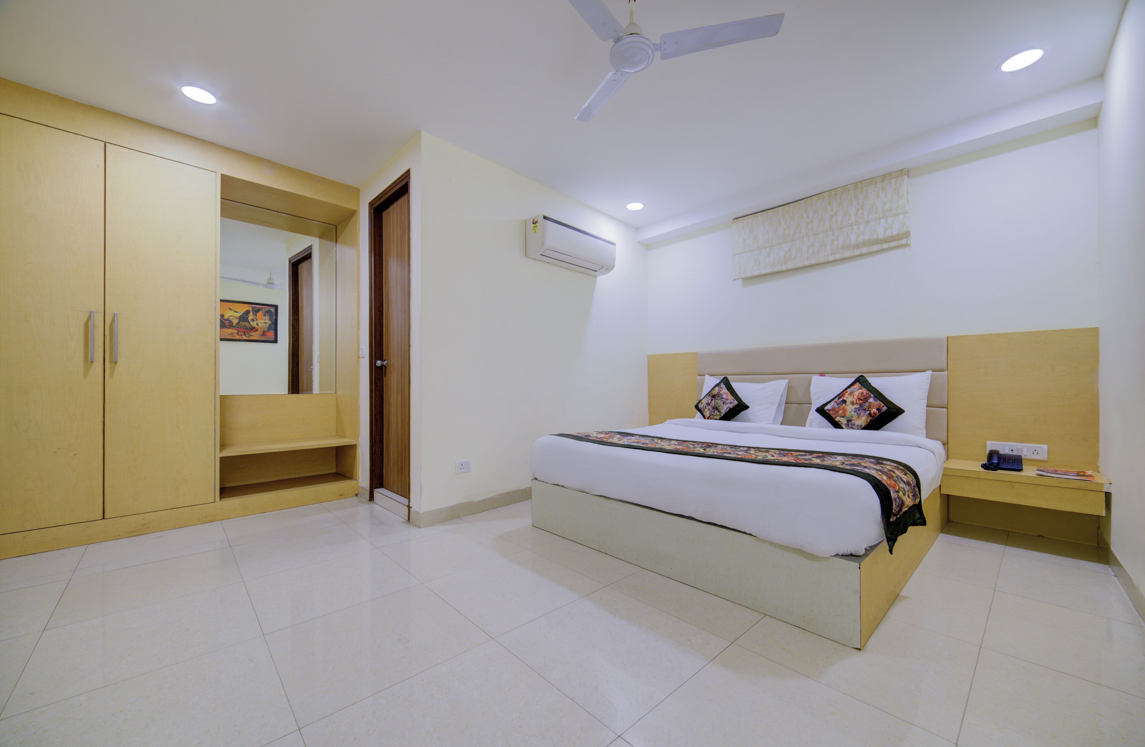 A bedroom with a bed, a wardrobe, a ceiling fan, an air conditioning unit, and a bedside table.