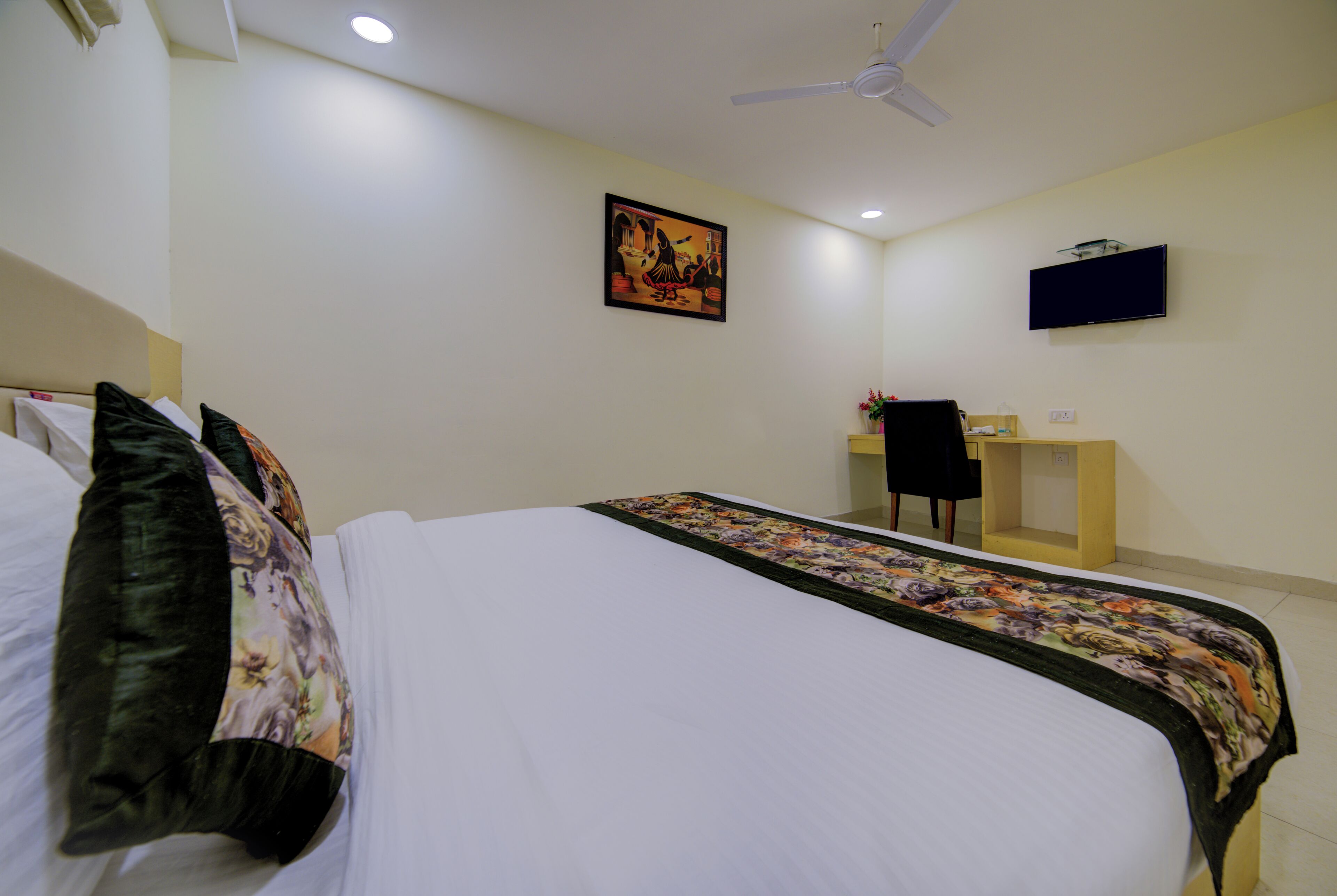 A hotel room with a bed, a desk, a chair, a television, and a ceiling fan.