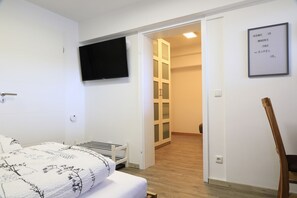 A bedroom with a bed, a TV mounted on the wall, a wooden chair, and a door leading to a hallway. - Ferienhaus Paulus (Schleiden)