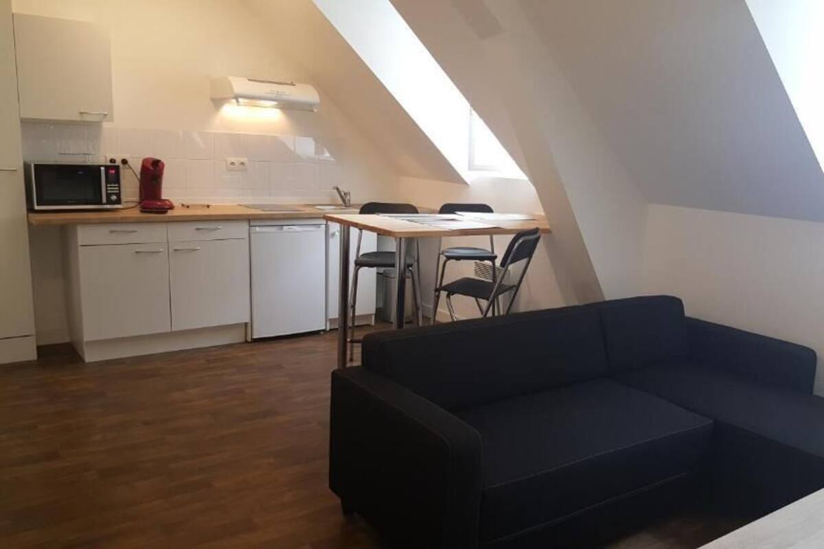 A loft-style apartment with a kitchen, dining area, and a dark-colored sofa.