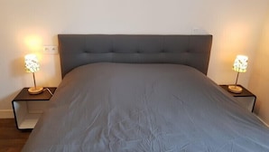 Un letto con una testiera grigia e due comodini con lampade.