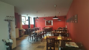 Una sala ristorante con diversi tavoli e sedie, pareti rosse e lampade a sospensione.