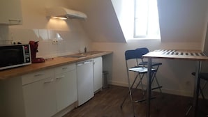 Una cucina compatta con mobili bianchi, un forno a microonde, una macchina del caffè rossa e un piccolo tavolo con una tastiera.
