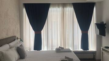 Una camera d'albergo con un letto grande, un comodino, una TV e una finestra con tende.