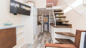 A narrow hallway with a wooden staircase and a flat-screen TV mounted on the wall. - Tiny House Siesta- perfect tiny house for two! (Sarasota)