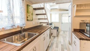 A kitchen with a wooden countertop, stainless steel sink, and a staircase leading to an upper level. - Tiny House Siesta- perfect tiny house for two! (Sarasota)