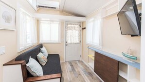 A compact room with a sofa, a television, and a small shelf with a model ship. - Tiny House Siesta- perfect tiny house for two! (Sarasota)