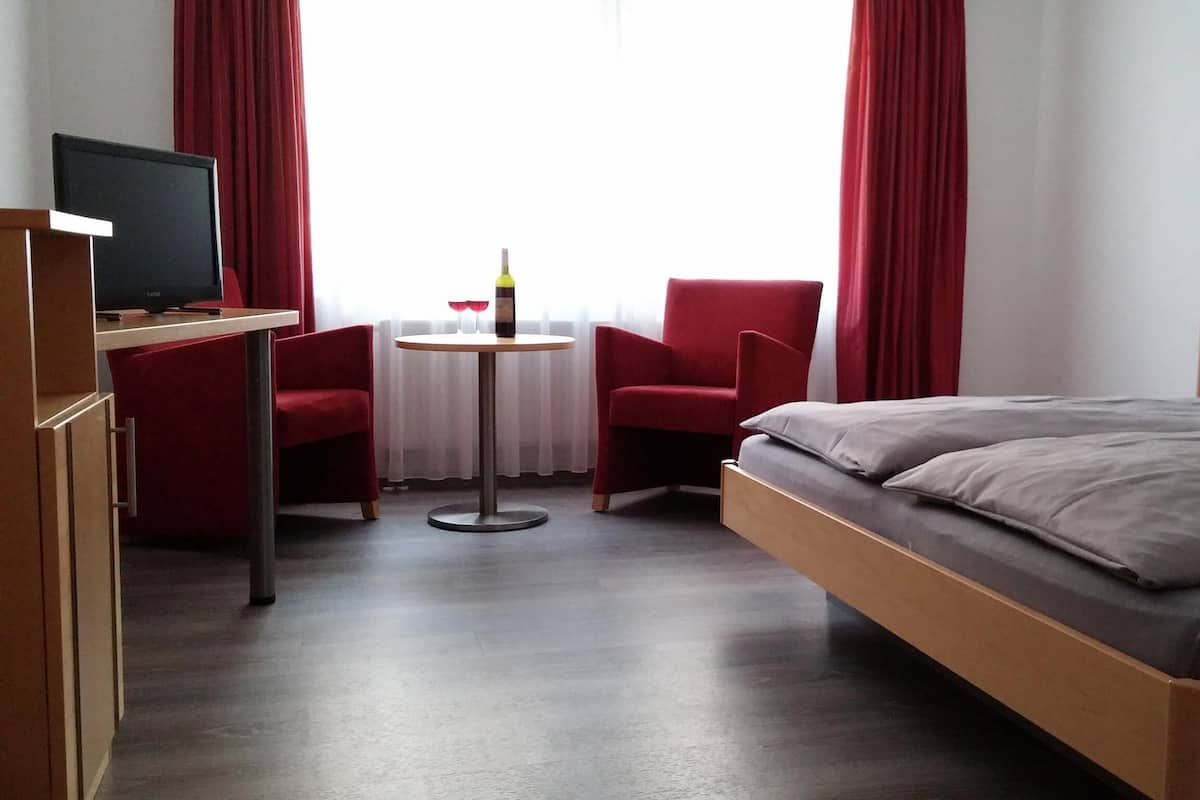 A hotel room with a bed, a TV, a desk, a chair, and a small table.