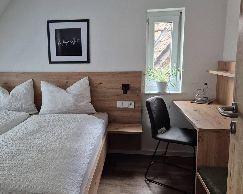 Quarto com cama, escrivaninha, cadeira, janela com planta e quadro na parede.