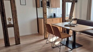 A dining area with a wooden table, two chairs, a fur rug, and a kitchen in the background.