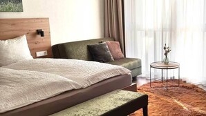 A bedroom with a bed, bench, sofa, and a small table with a vase.