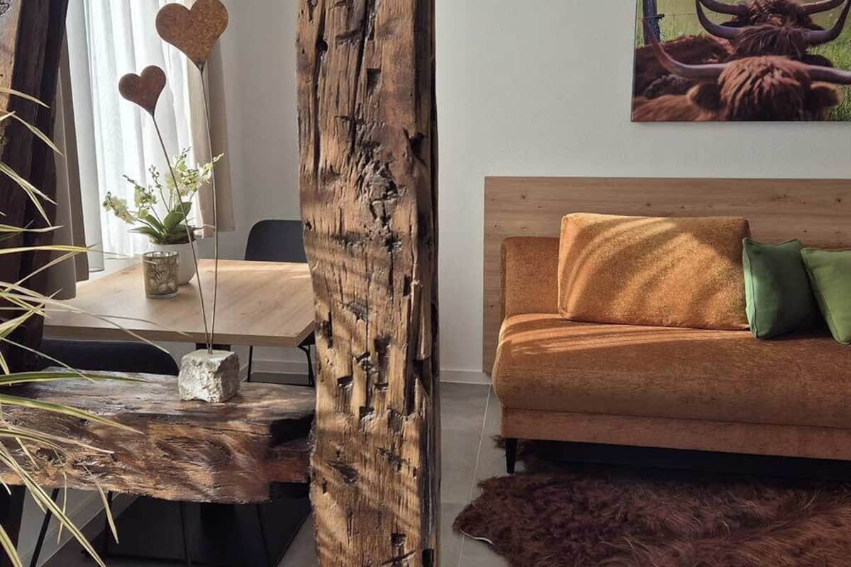 A room with a wooden dining table, a sofa with cushions, a painting of a bull, and a rustic wooden pillar.