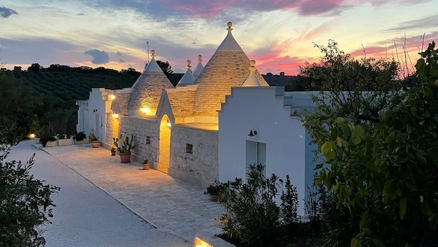 Filas de edificios blancos con techos cónicos, un camino de grava y un cielo al atardecer.