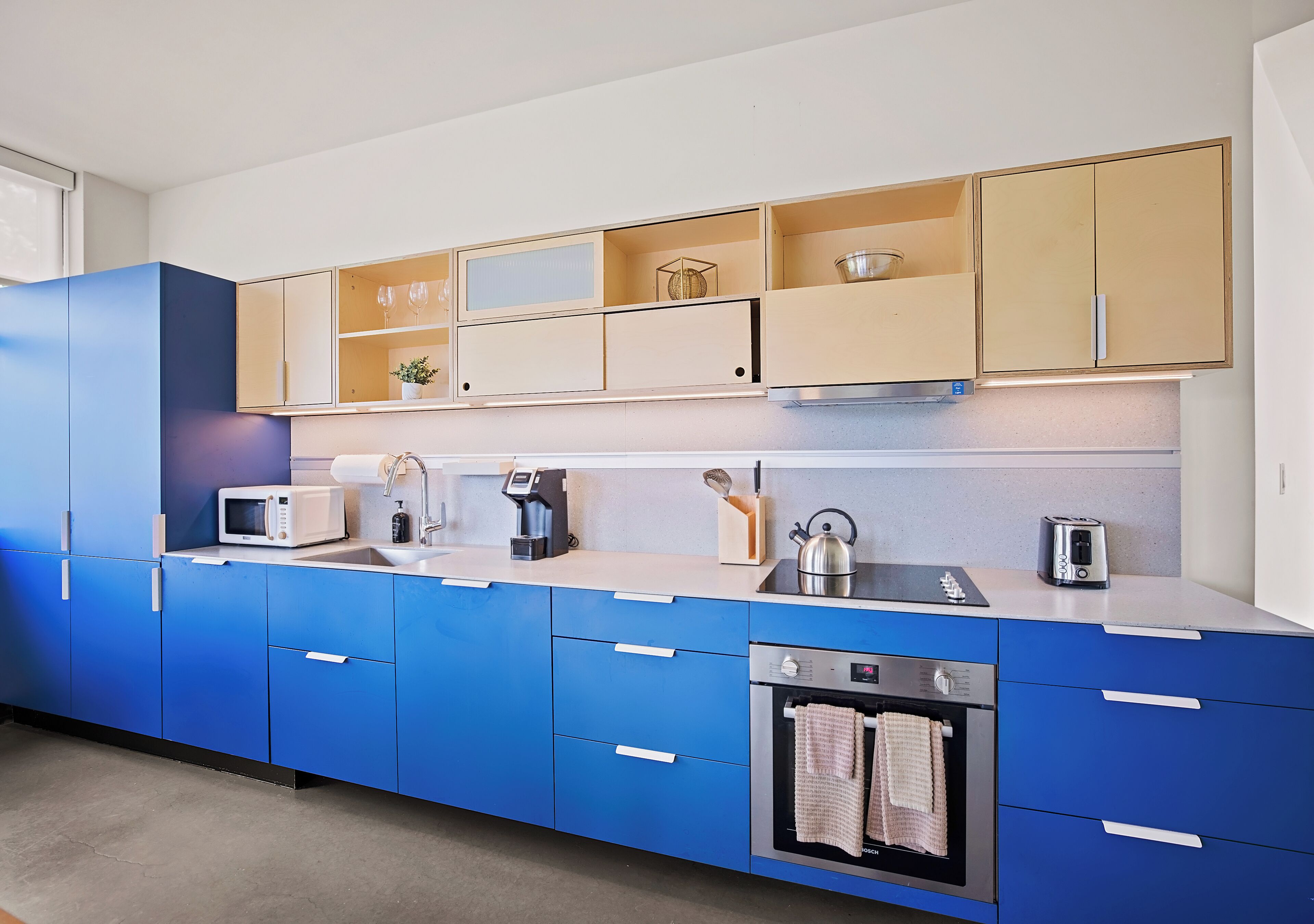 A modern kitchen with blue cabinets, a microwave, a kettle, and a toaster.
