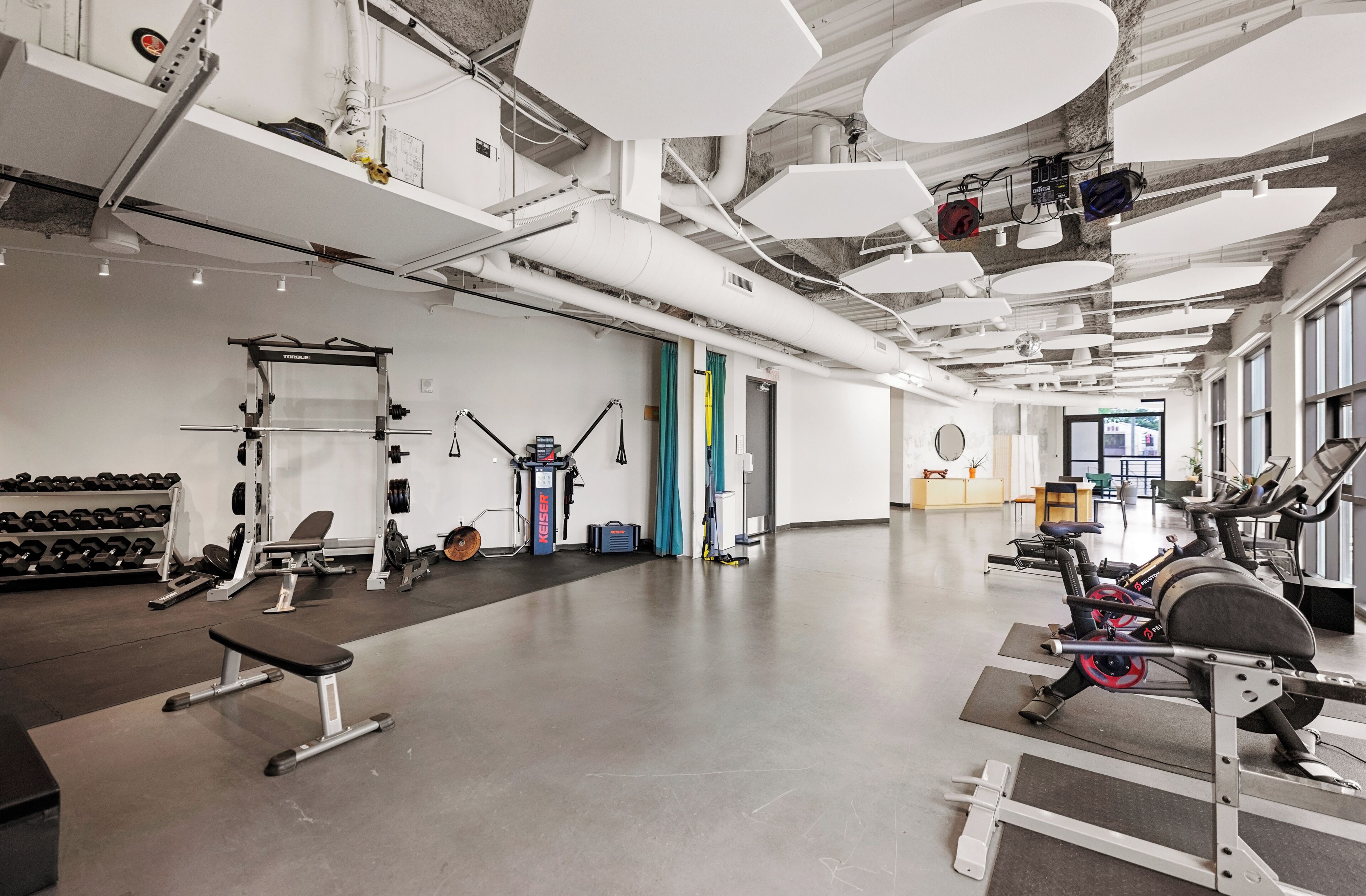 Ein Fitnessraum mit Trainingsgeräten, einer Bank, Kurzhanteln und einem Laufband.