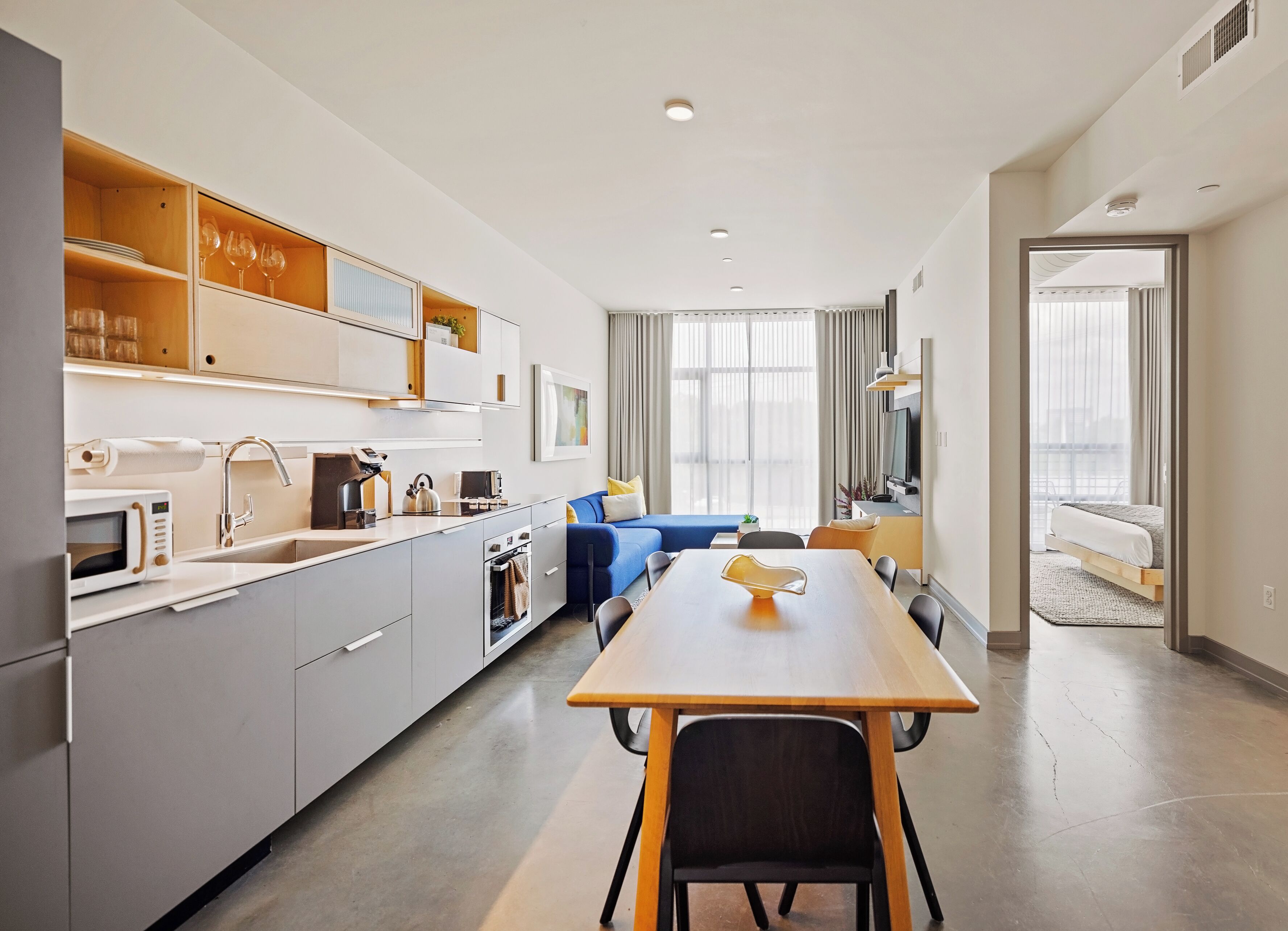 Una cocina moderna con electrodomésticos integrados, una zona de comedor con mesa de madera y un salón con sofá azul.