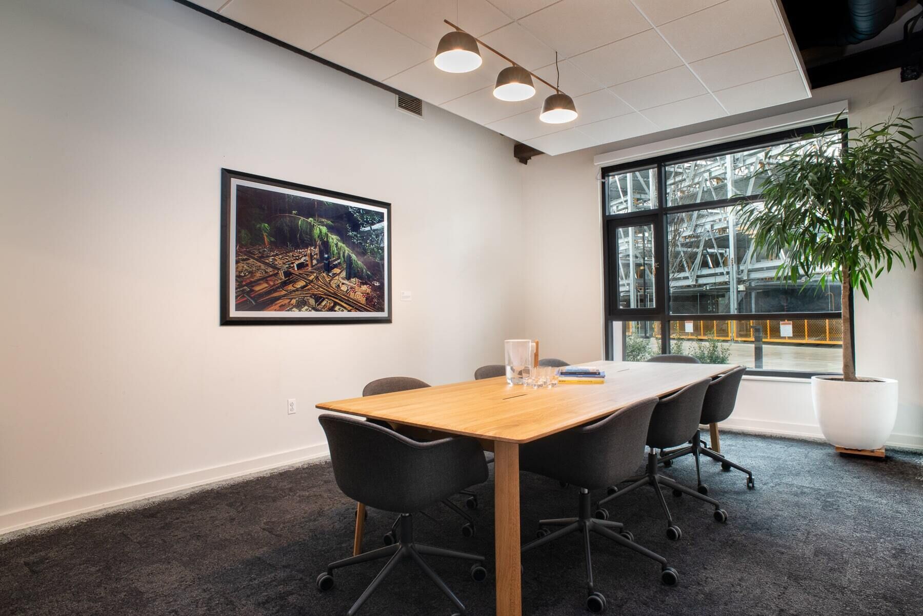 A conference room with a long table, four chairs, a large window, and a framed picture on the wall.