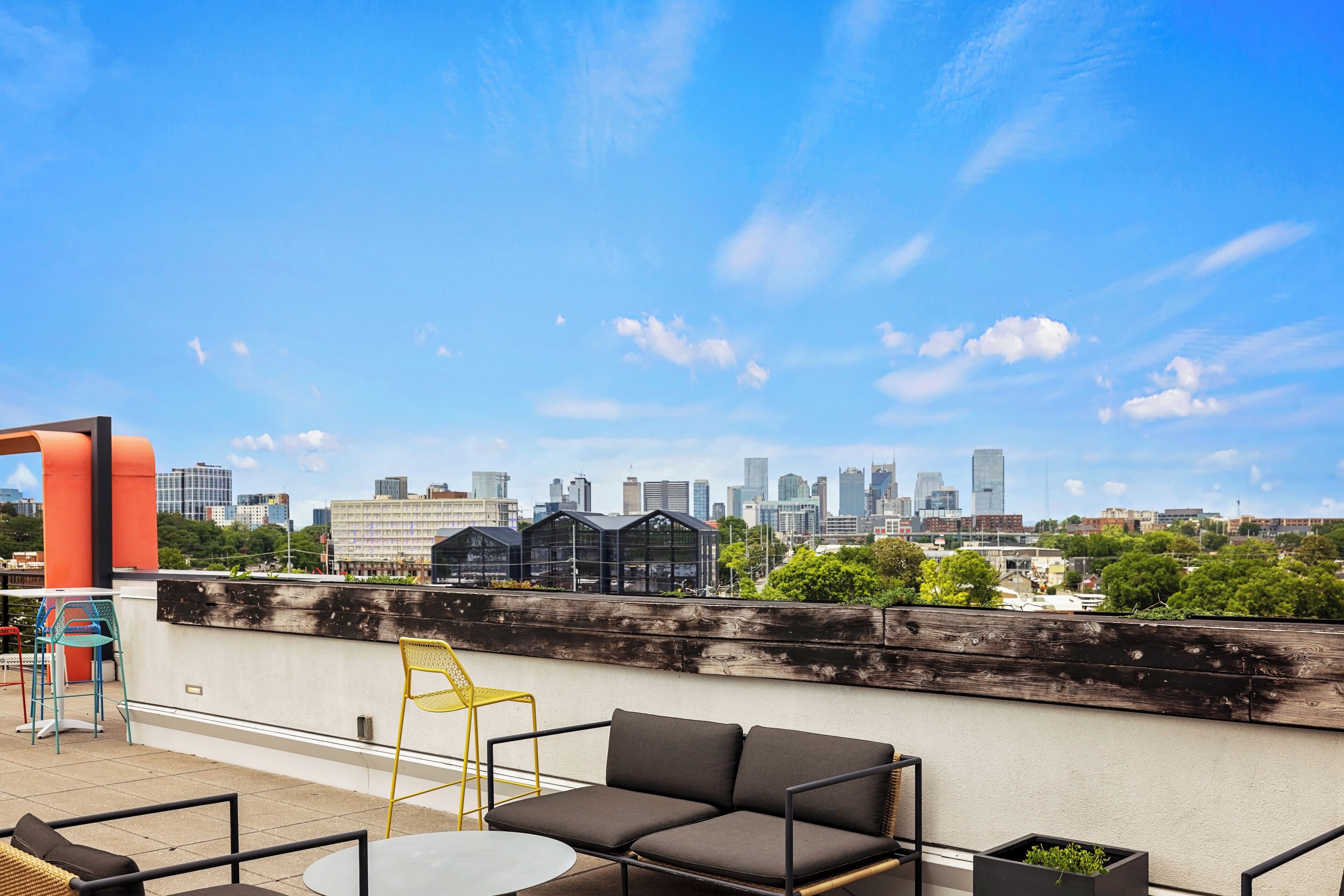 A rooftop terrace with a city skyline view, a sofa, chairs, and a small table.