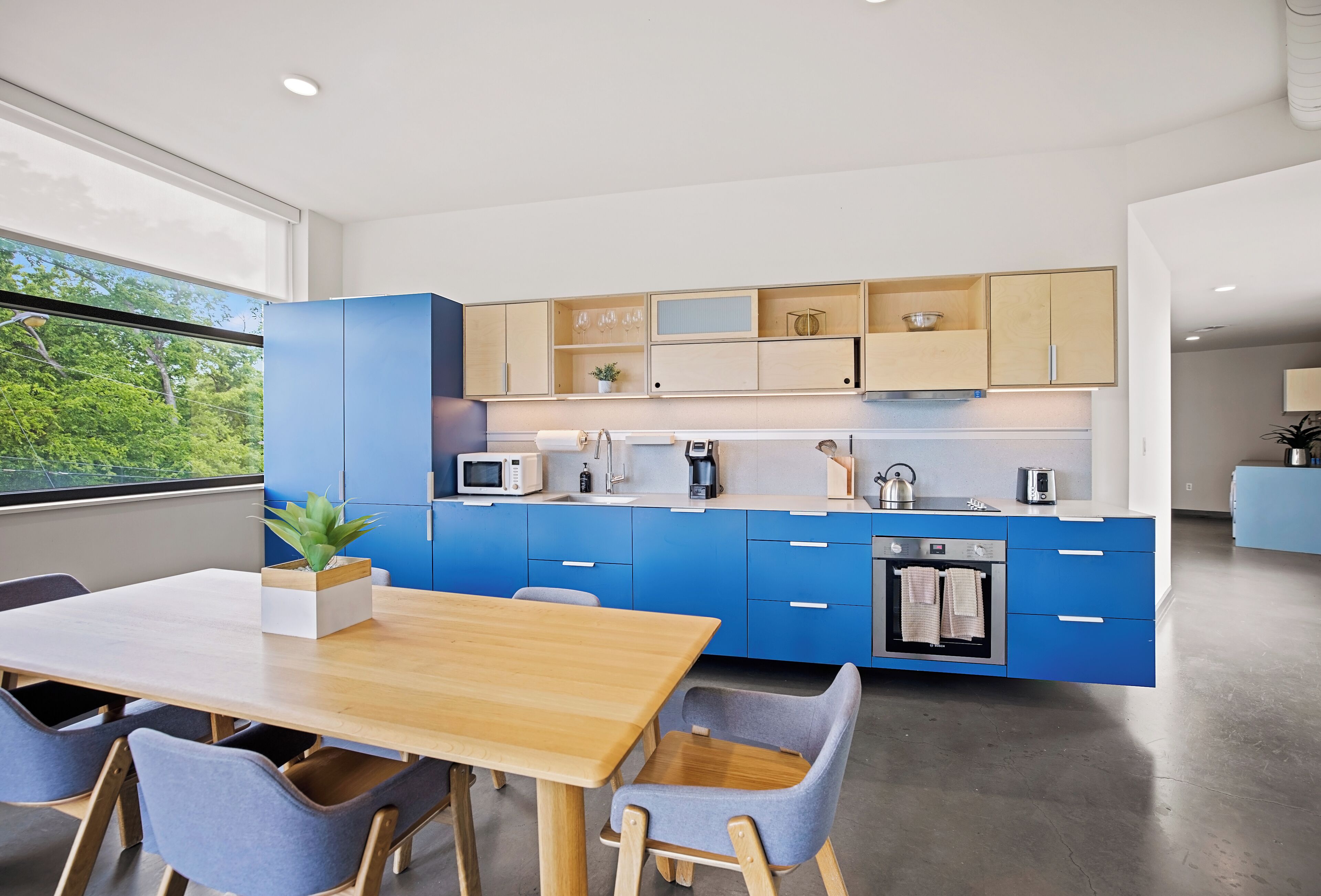 A modern kitchen with blue cabinets, a wooden dining table, and chairs.