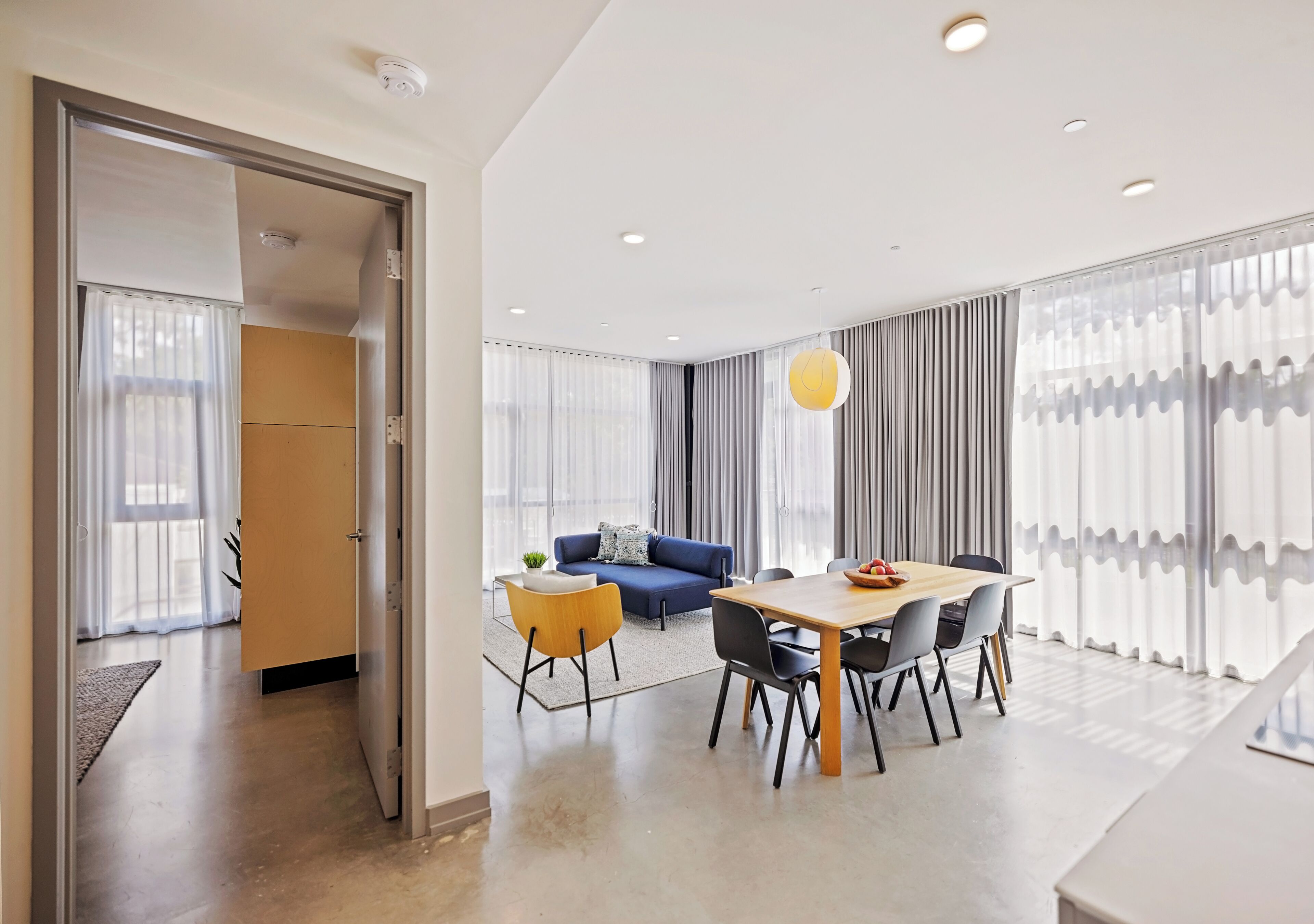 A modern hotel room with a dining area, a sofa, and a large window with curtains.
