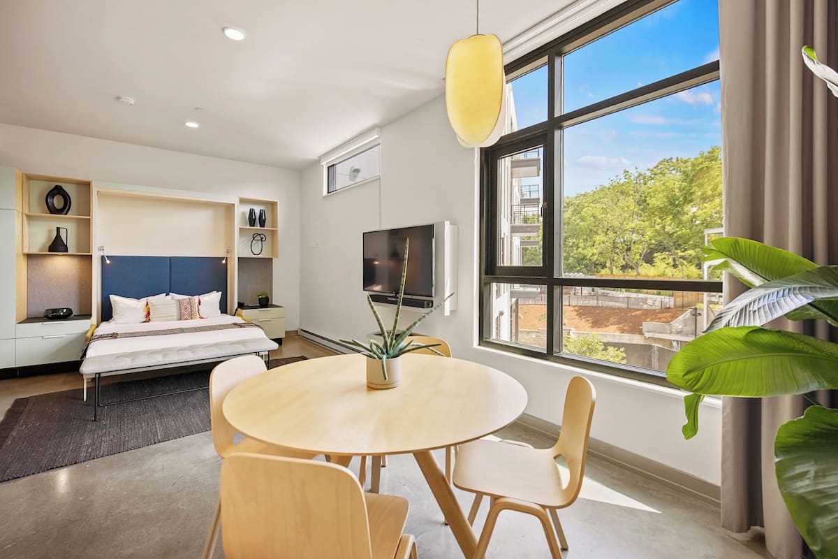 Une chambre d’hôtel moderne équipée d’un lit, d’une télévision, d’une table à manger et d’une grande fenêtre donnant sur la ville.