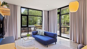 A modern living room with a blue sofa, large windows, and a view of the outdoors. - Harthall Hotel (Nashville)