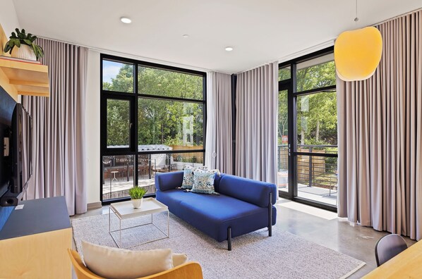 Una sala de estar moderna con un sofá azul, ventanas amplias y vistas al exterior.