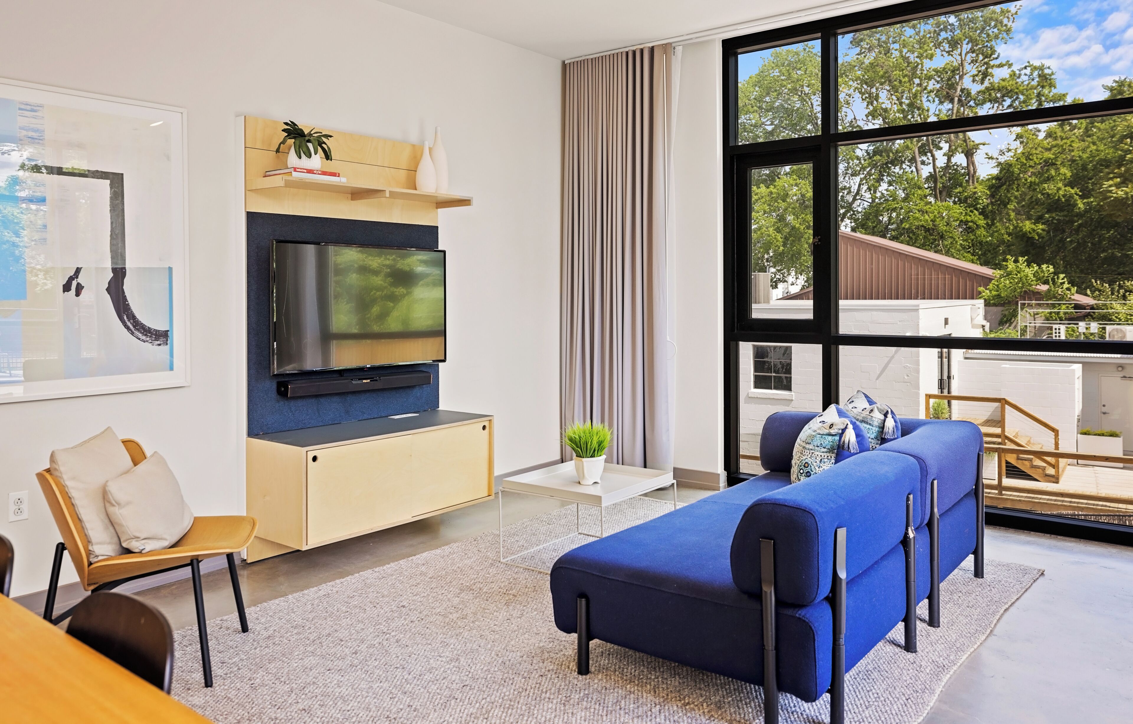 A modern living room with a large TV, a sofa, a coffee table, and a view of the outdoors.
