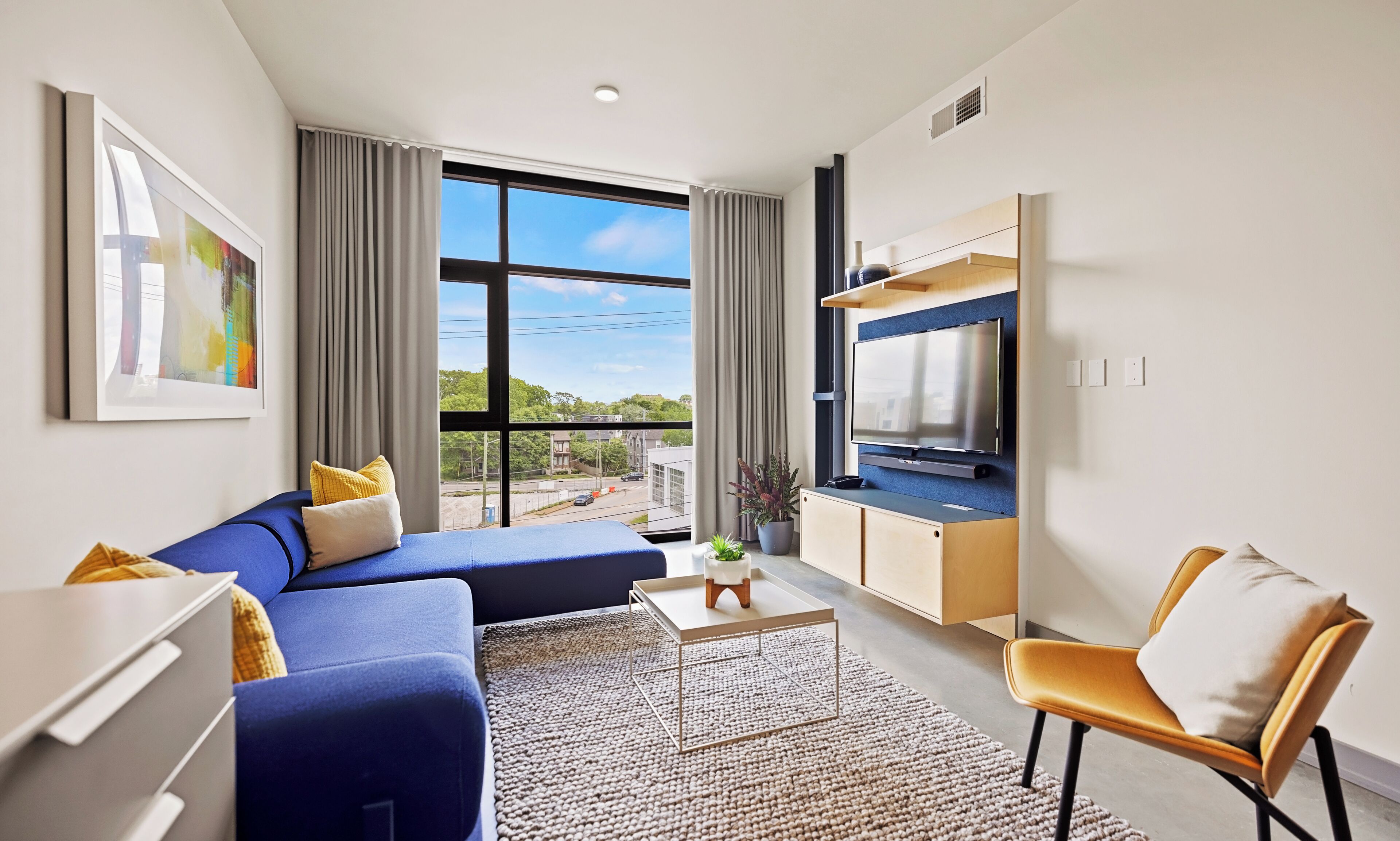 A modern living room with a sofa, a chair, a TV, and a large window offering a city view.