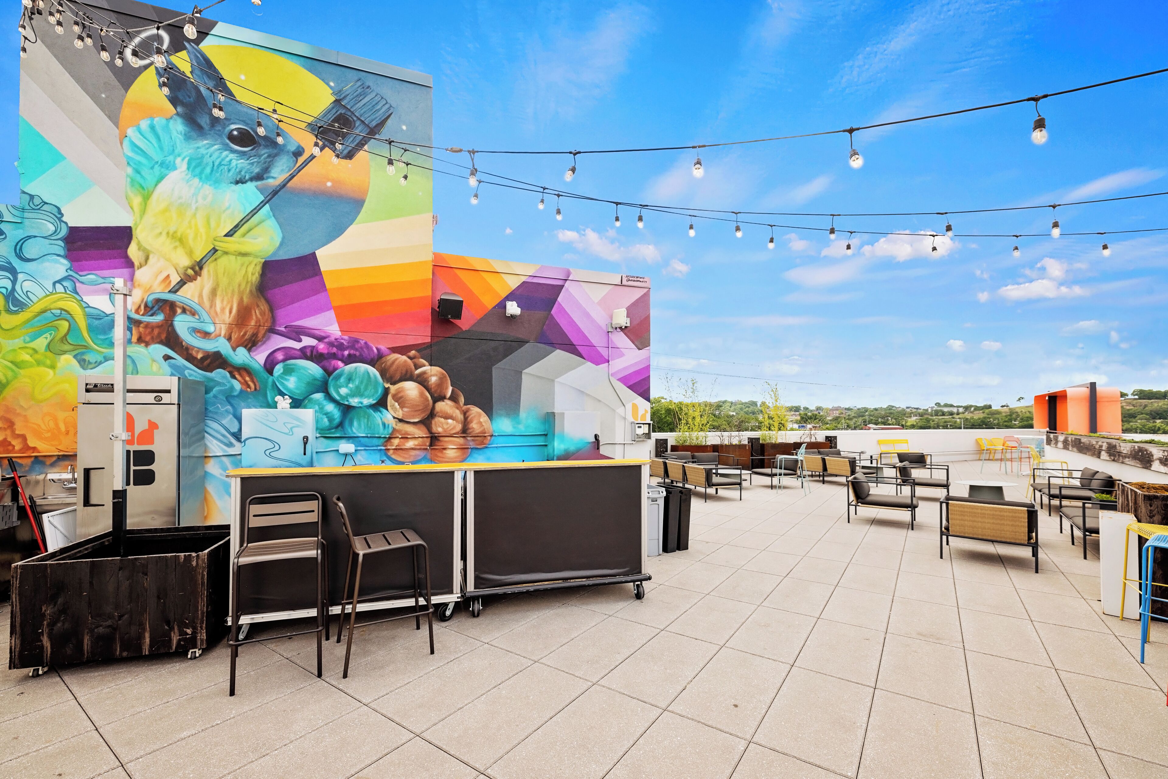 A rooftop terrace with outdoor seating, a mural, and string lights.