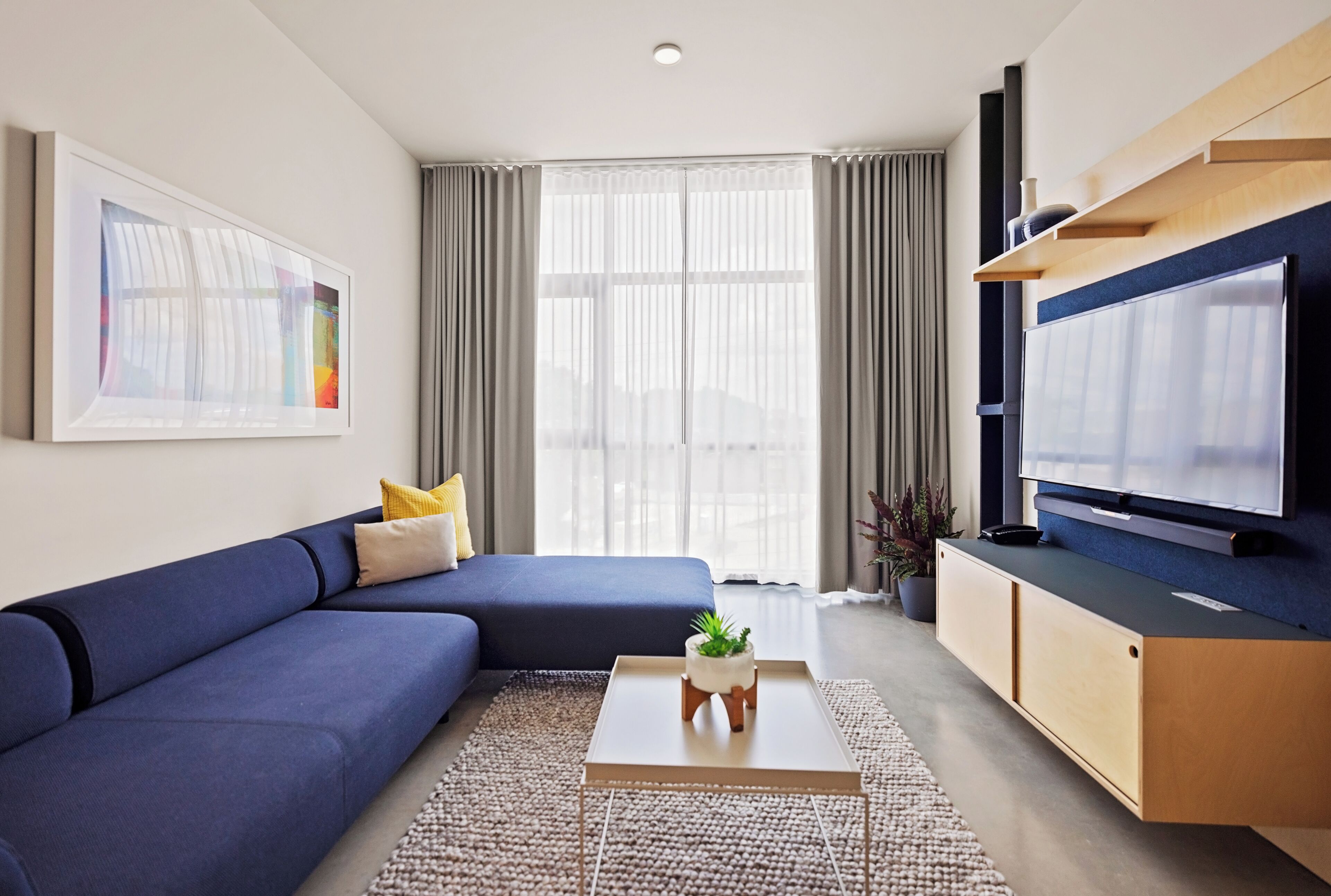 A modern living room with a sofa, coffee table, TV, and a large window with curtains.
