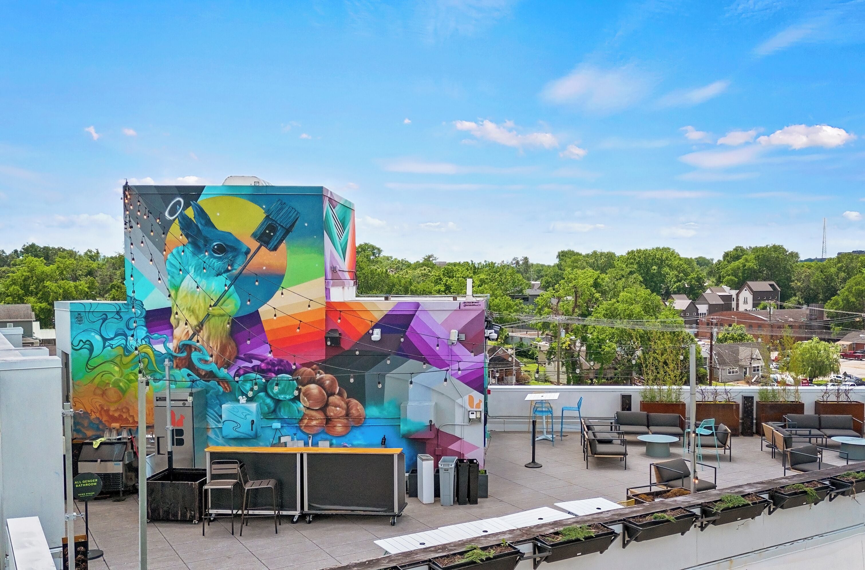 A rooftop terrace with outdoor seating, a mural, and a view of the surrounding area.