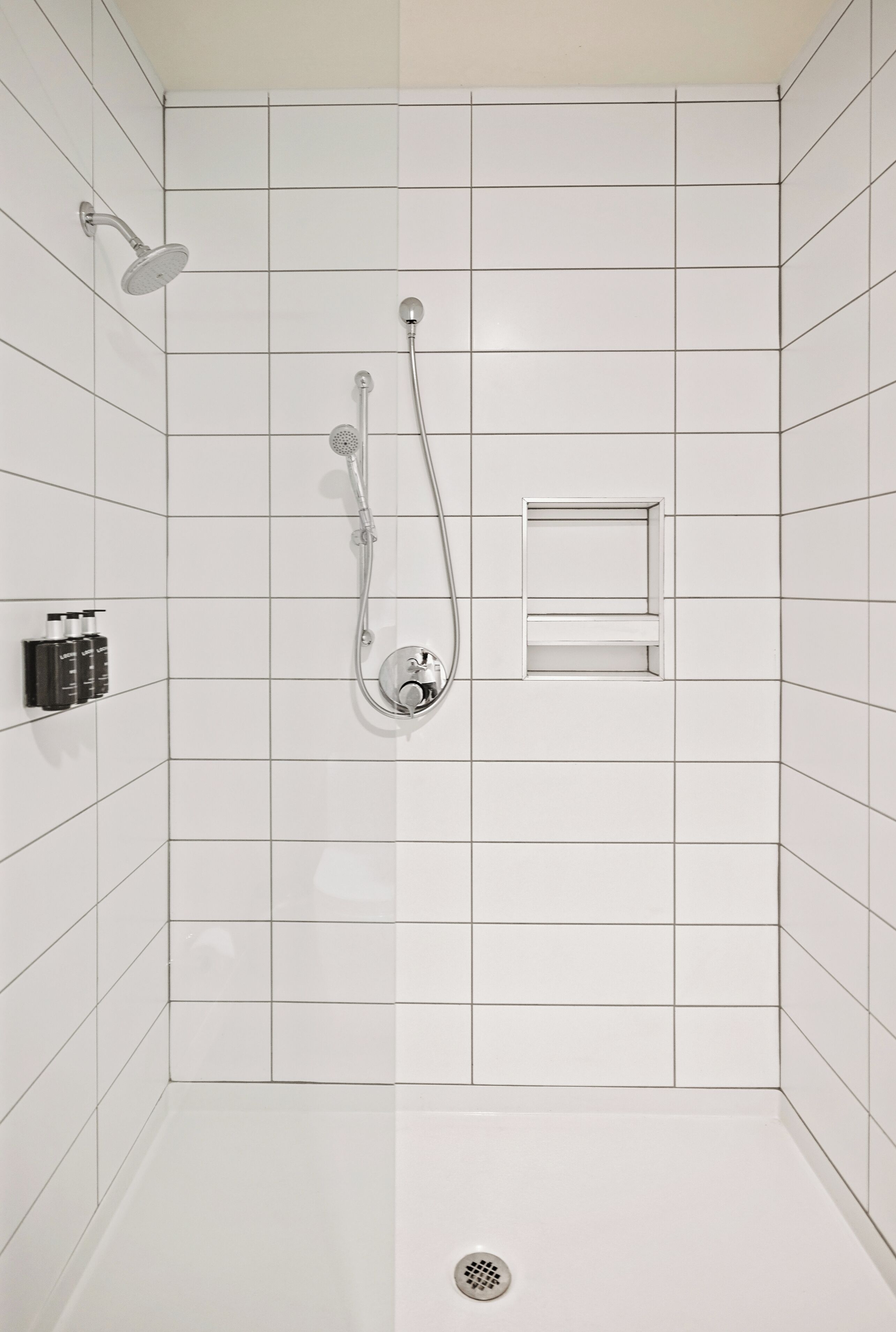 Een douche met een handdouche, een wandmengkraan en een klein plankje met toiletartikelen.