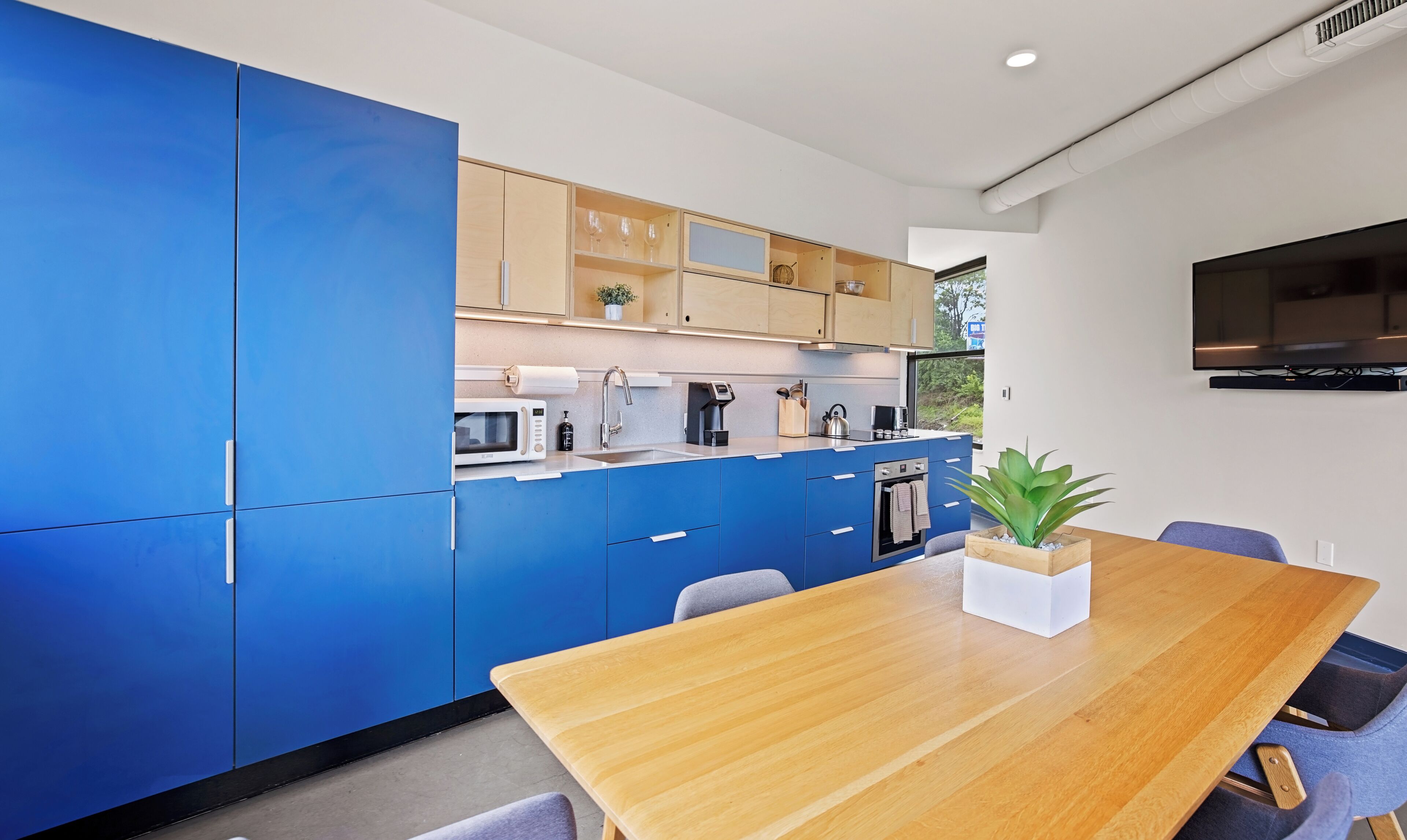 Une cuisine moderne avec des meubles de rangement bleus, une table à manger en bois et une grande fenêtre.