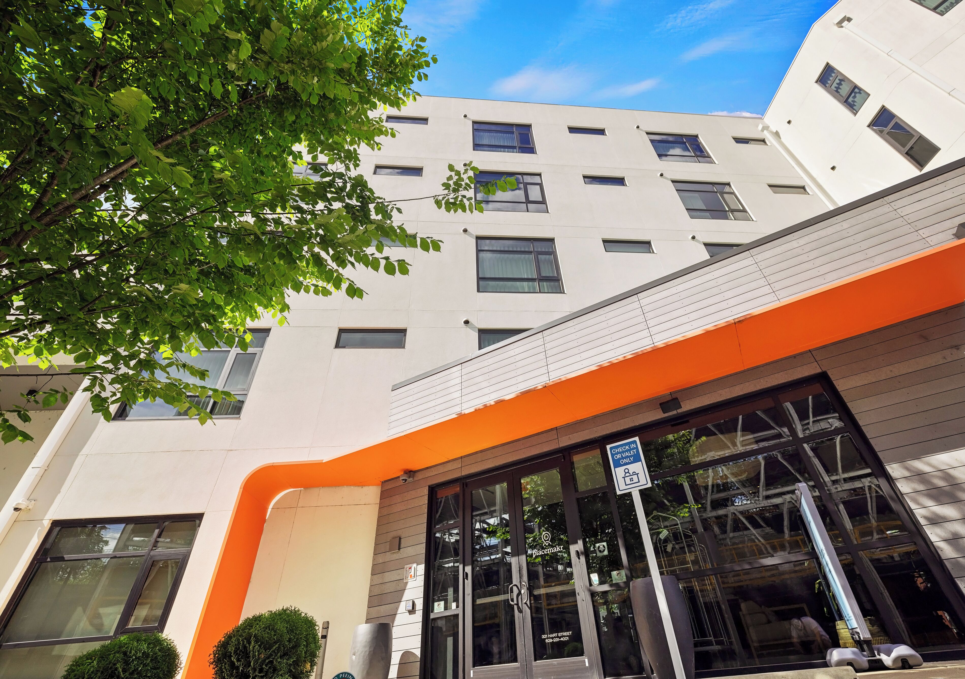 Un edificio moderno con fachada blanca, ventanas grandes y detalles en color naranja.